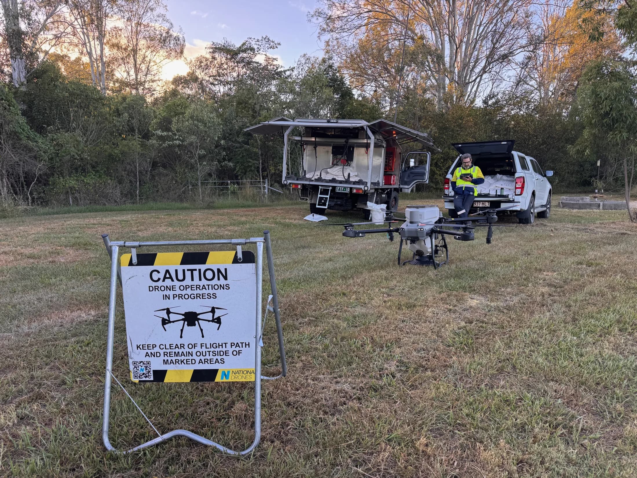 National Drones field setup with safety sign, application aircraft, operator, and support vehicles