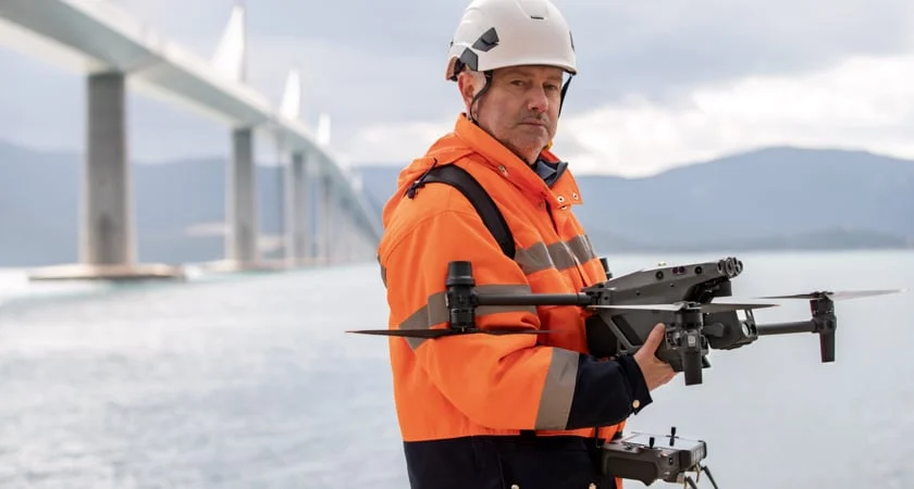 Field operator preparing a Matrice 30 Series aircraft beside a bridge.