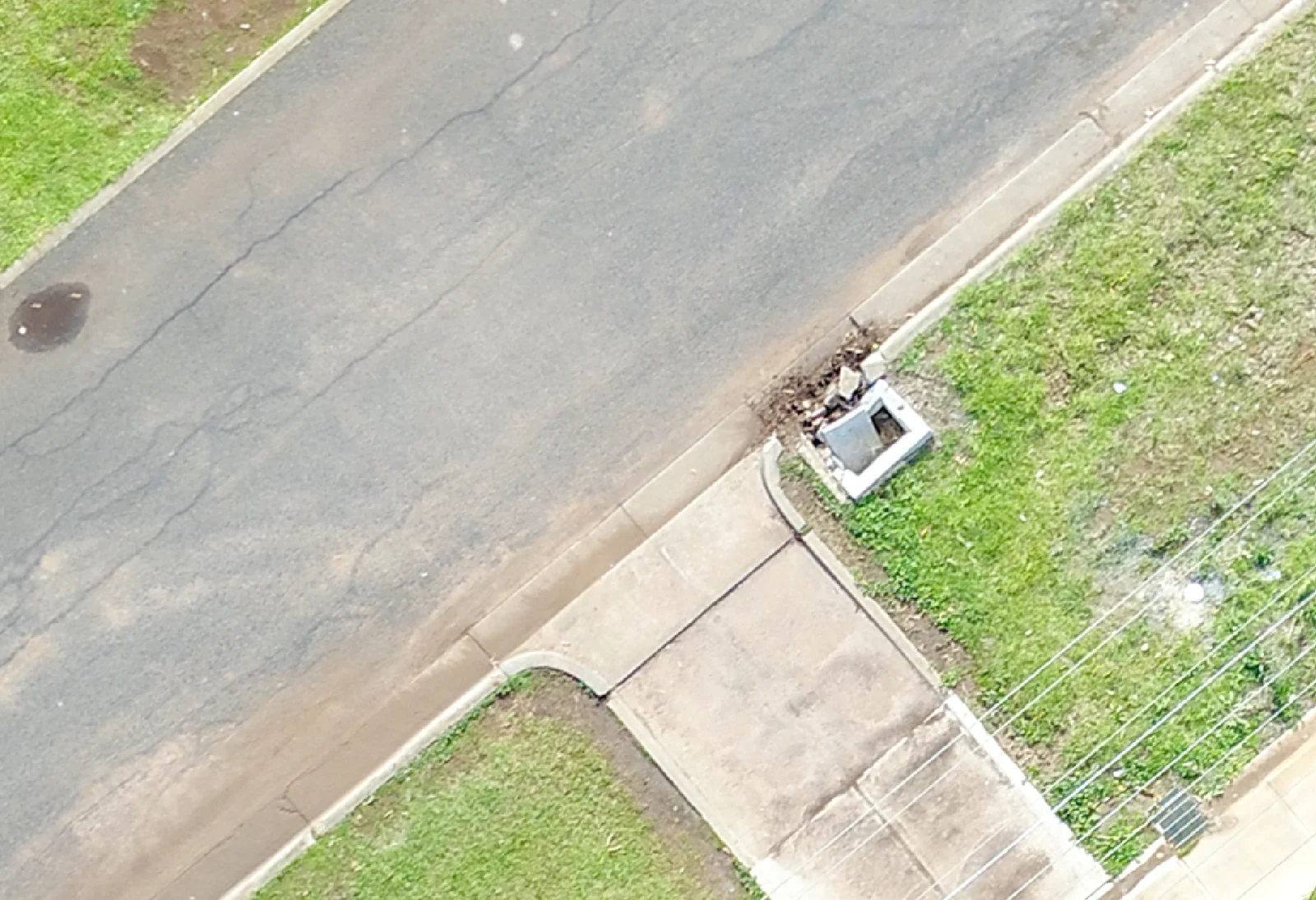 Aerial detail of a drain cover and surrounding pavement beside a road