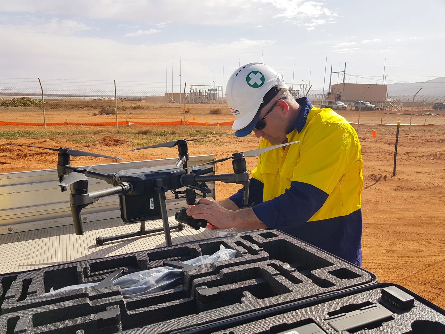 Operator preparing a multirotor drone beside its equipment case at a field site